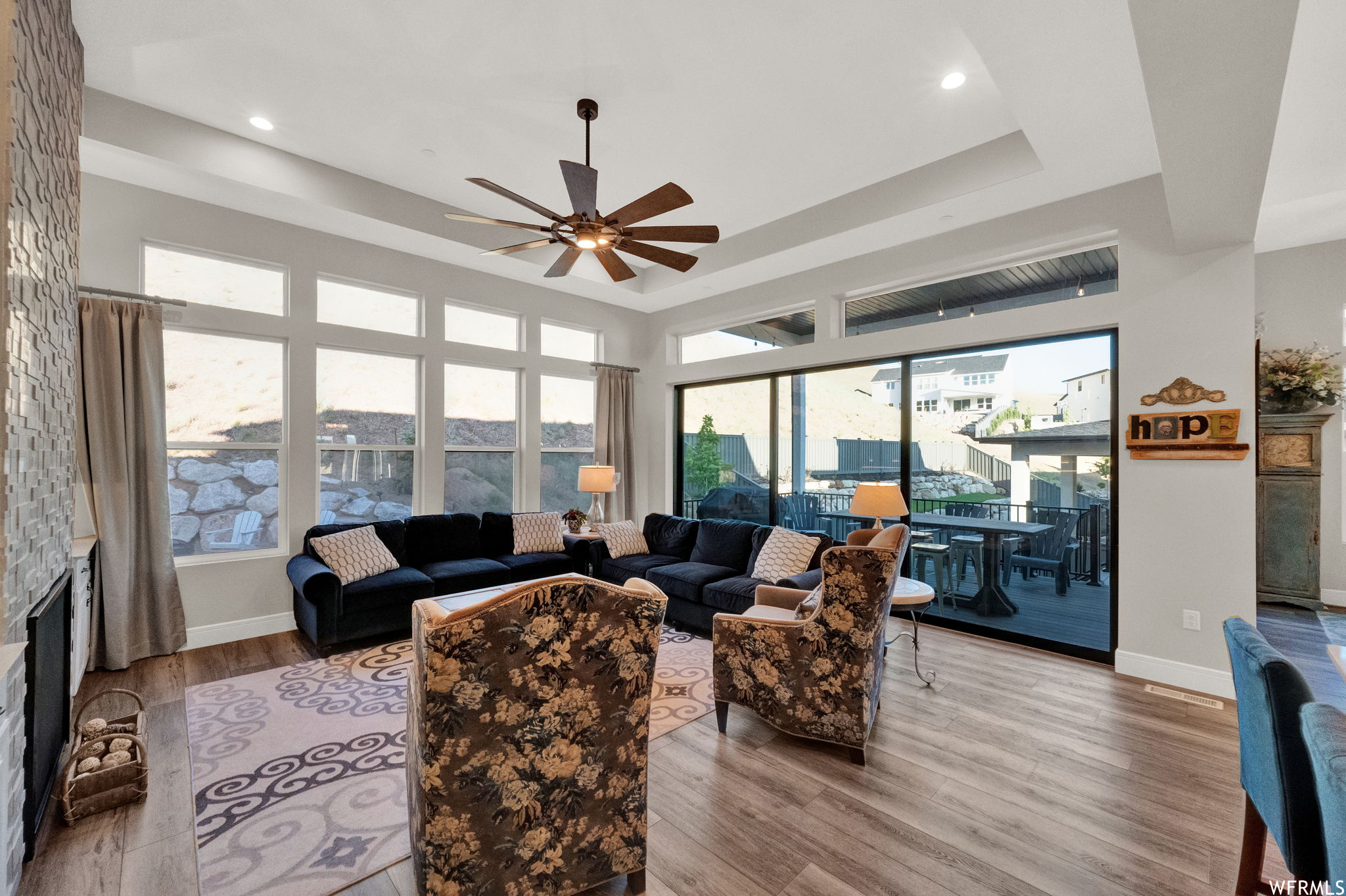 Living room featuring light hardwood floors, a raised ceiling, and ceiling fan
