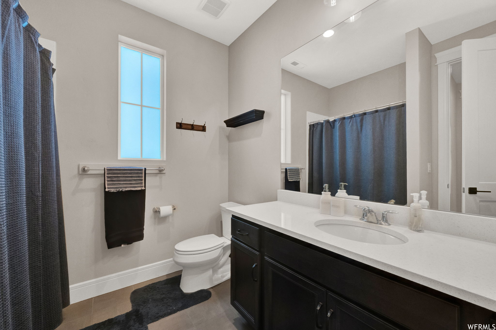 Bathroom featuring mirror, vanity with extensive cabinet space, tile floors, and a wealth of natural light
