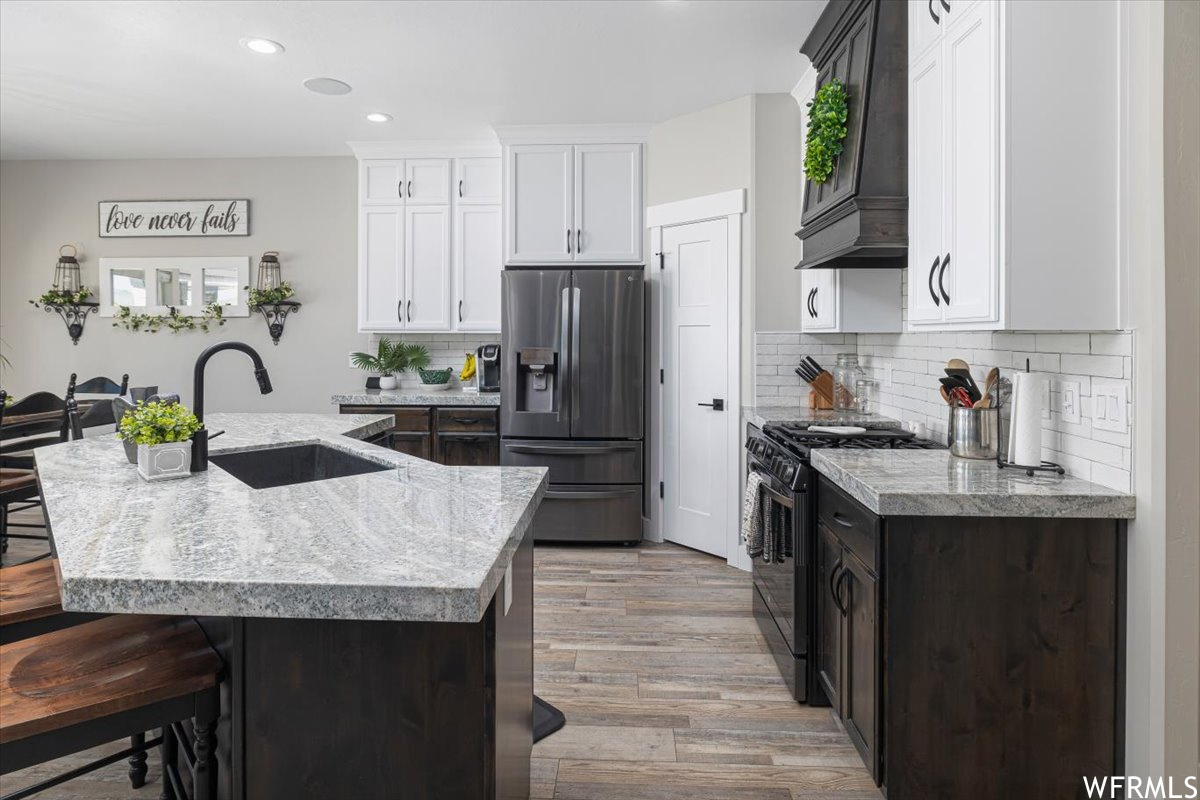 Kitchen featuring stainless steel fridge, light hardwood / wood-style floors, a breakfast bar area, gas range oven, and sink