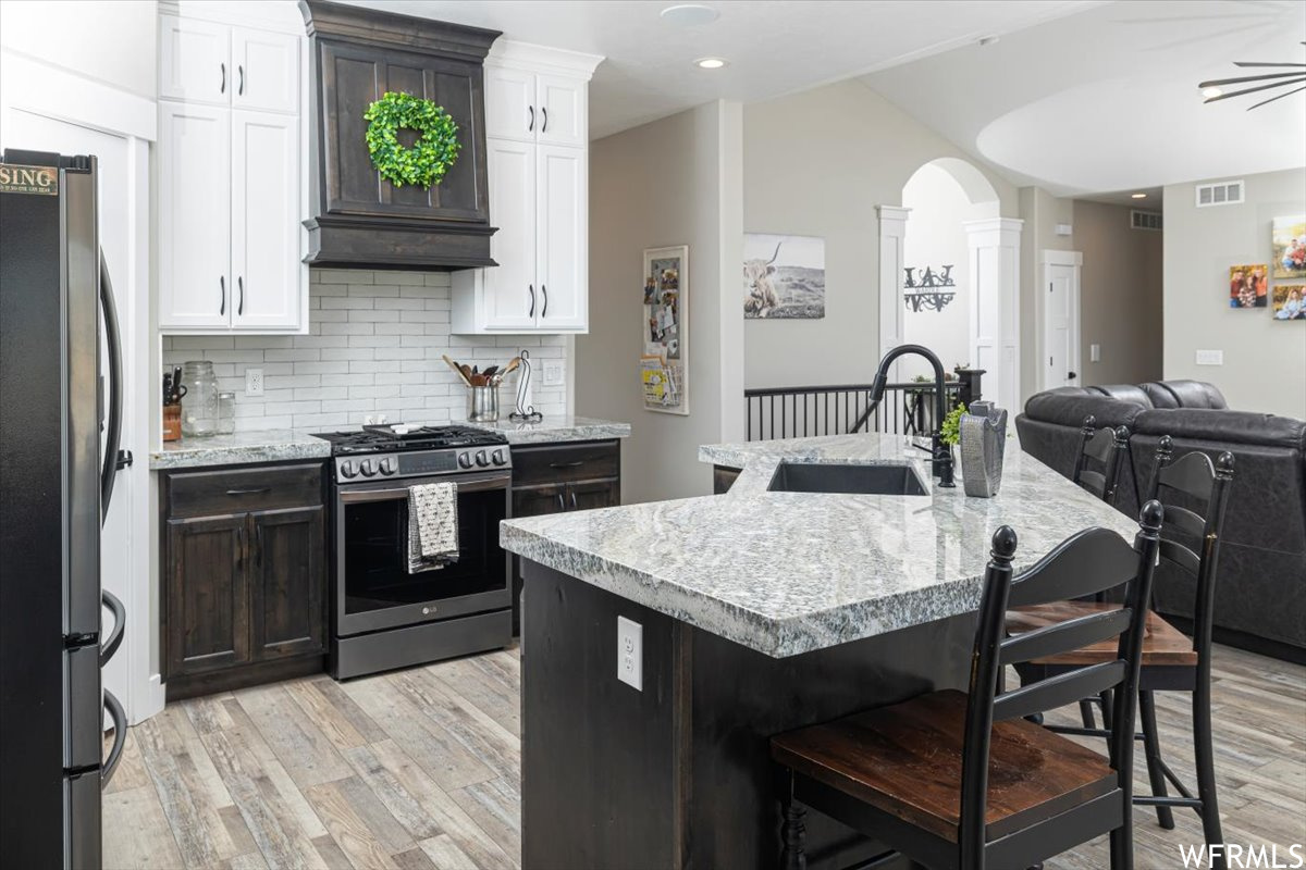 Kitchen featuring light hardwood / wood-style flooring, premium range hood, stainless steel appliances, sink, and decorative columns