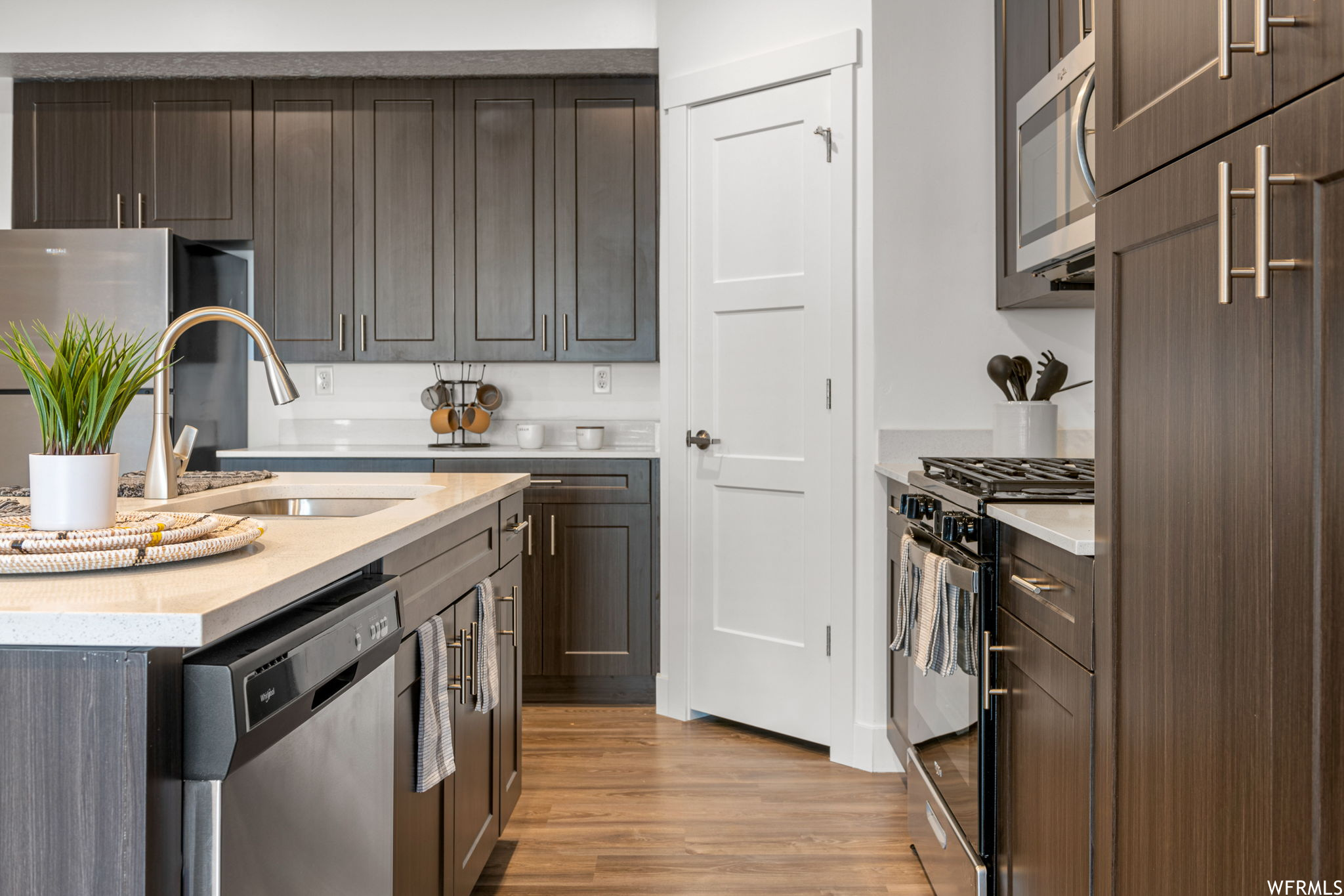 Kitchen featuring dark brown cabinetry, appliances with stainless steel finishes, light countertops, and light hardwood flooring