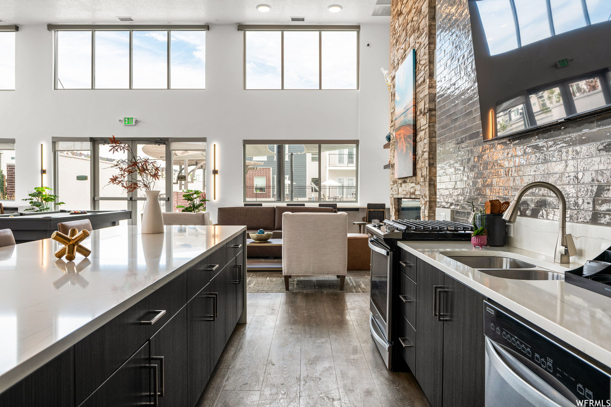 Kitchen featuring dark brown cabinets, light countertops, light hardwood flooring, dishwashing machine, a high ceiling, and stainless steel range with gas stovetop