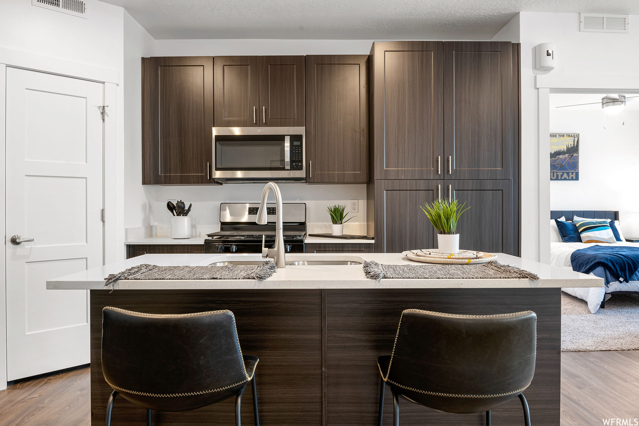 Kitchen with stainless steel appliances, a center island, light countertops, dark brown cabinets, and light hardwood floors