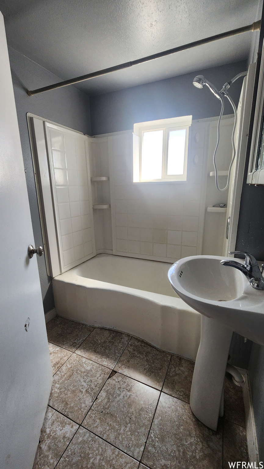 Bathroom featuring washbasin, tiled shower / bath, tile flooring, and a textured ceiling