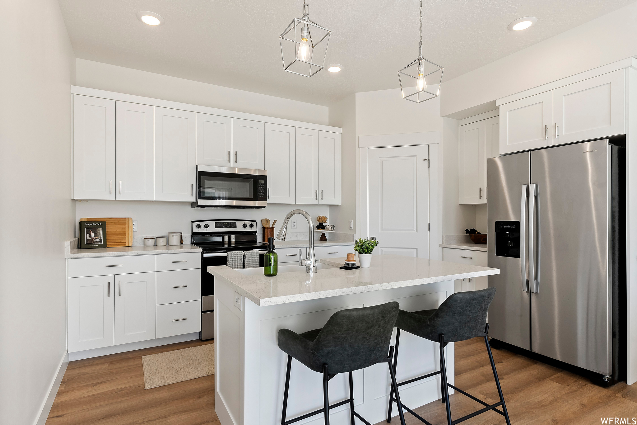 Kitchen with pendant lighting, light wood-type flooring, white cabinets, and stainless steel appliances