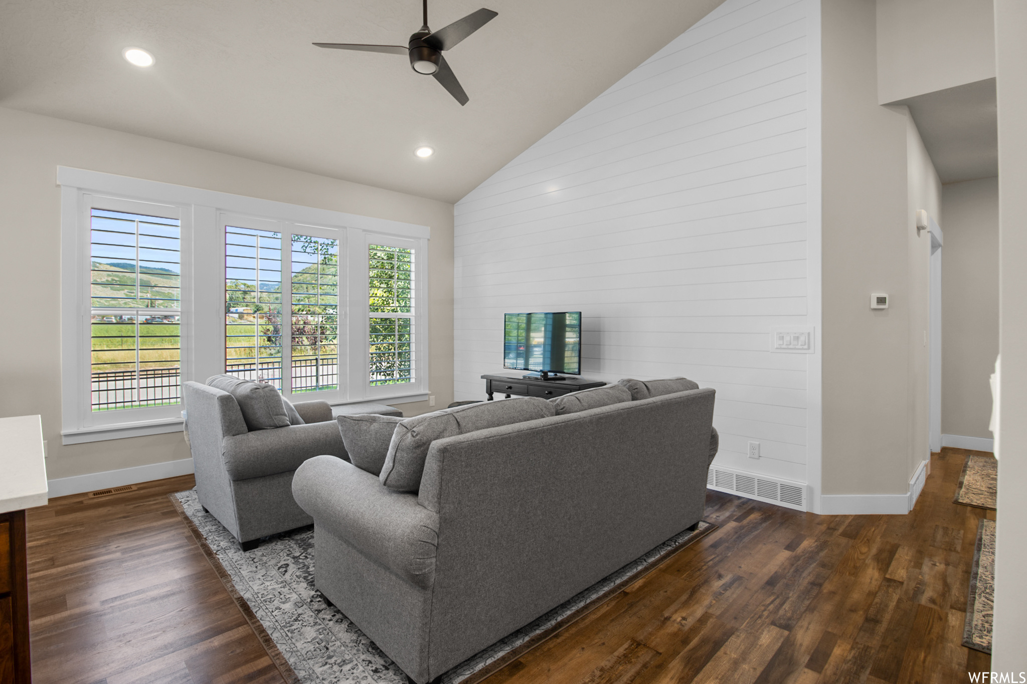 Hardwood floored living room with vaulted ceiling, a high ceiling, and ceiling fan