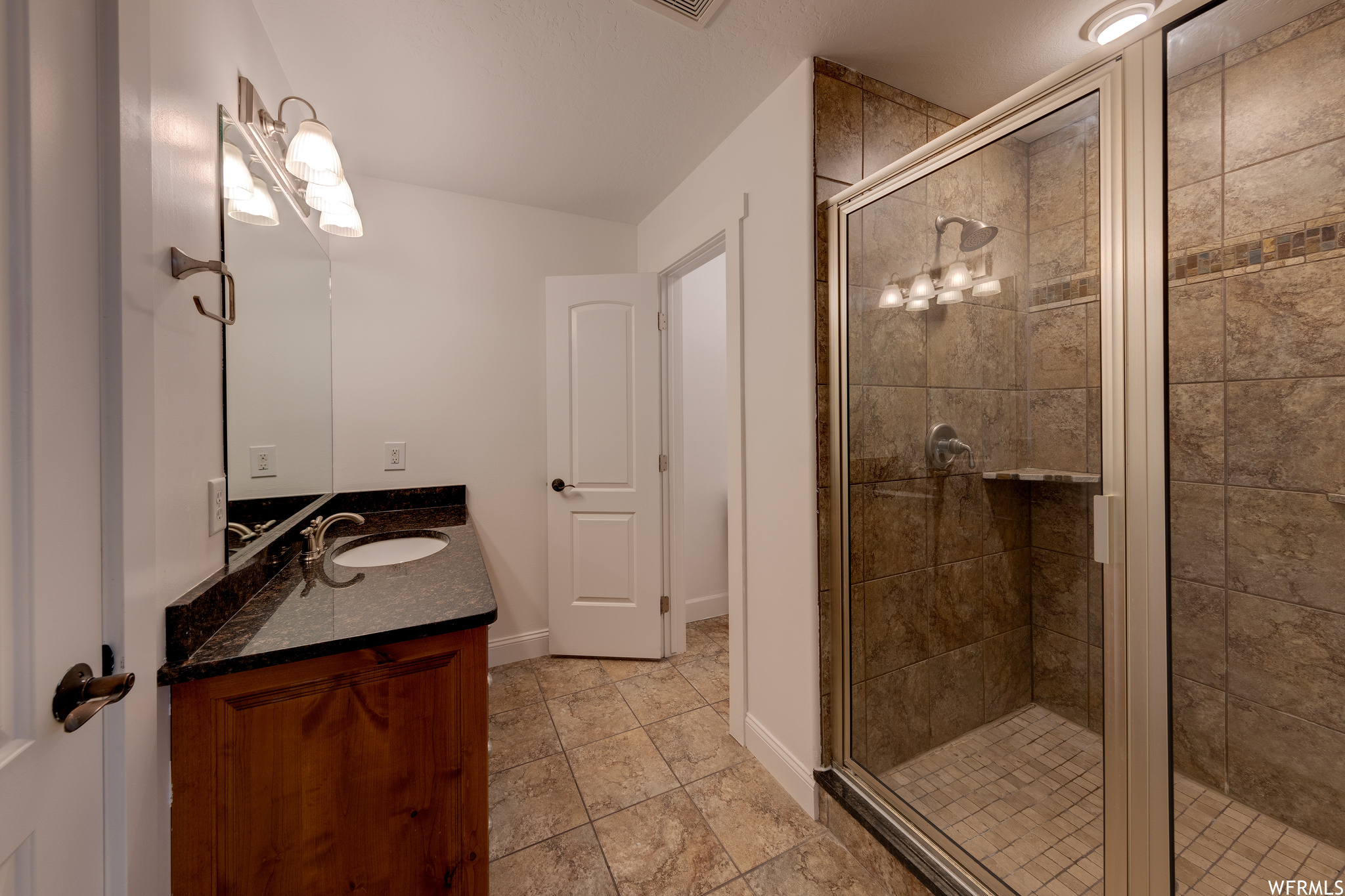 Bathroom featuring vanity with extensive cabinet space, mirror, a shower with door, and light tile floors