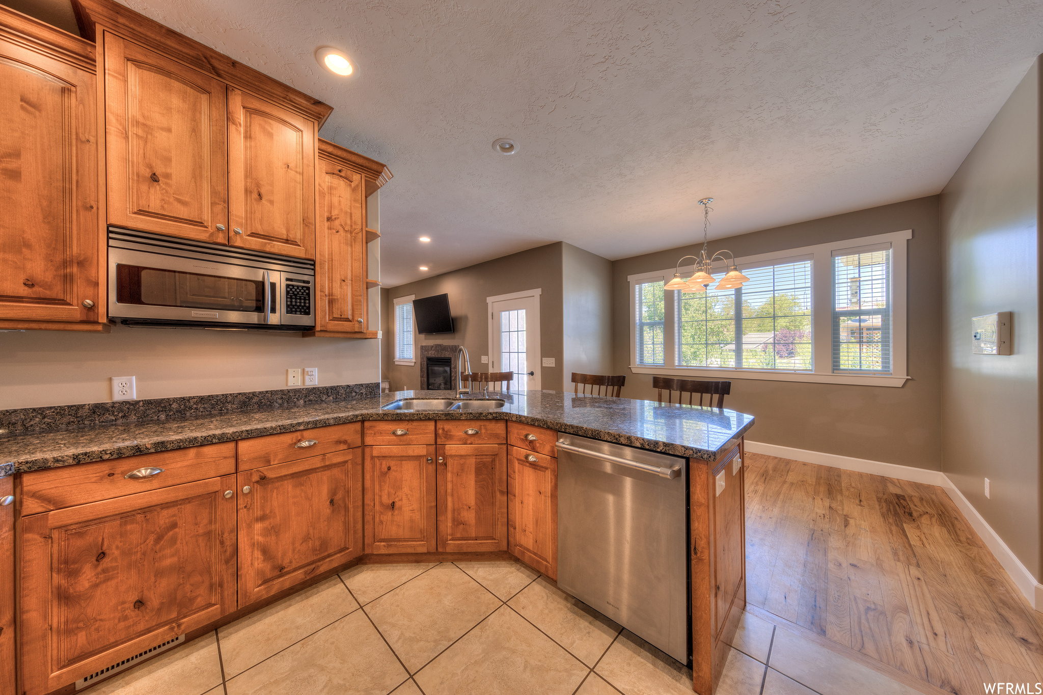 Kitchen featuring appliances with stainless steel finishes, a textured ceiling, light tile flooring, dark stone countertops, and brown cabinets