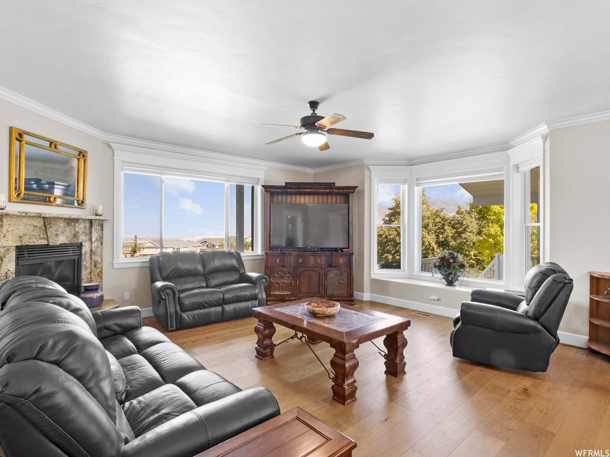 Living room featuring ceiling fan, light hardwood flooring, a fireplace, and crown molding
