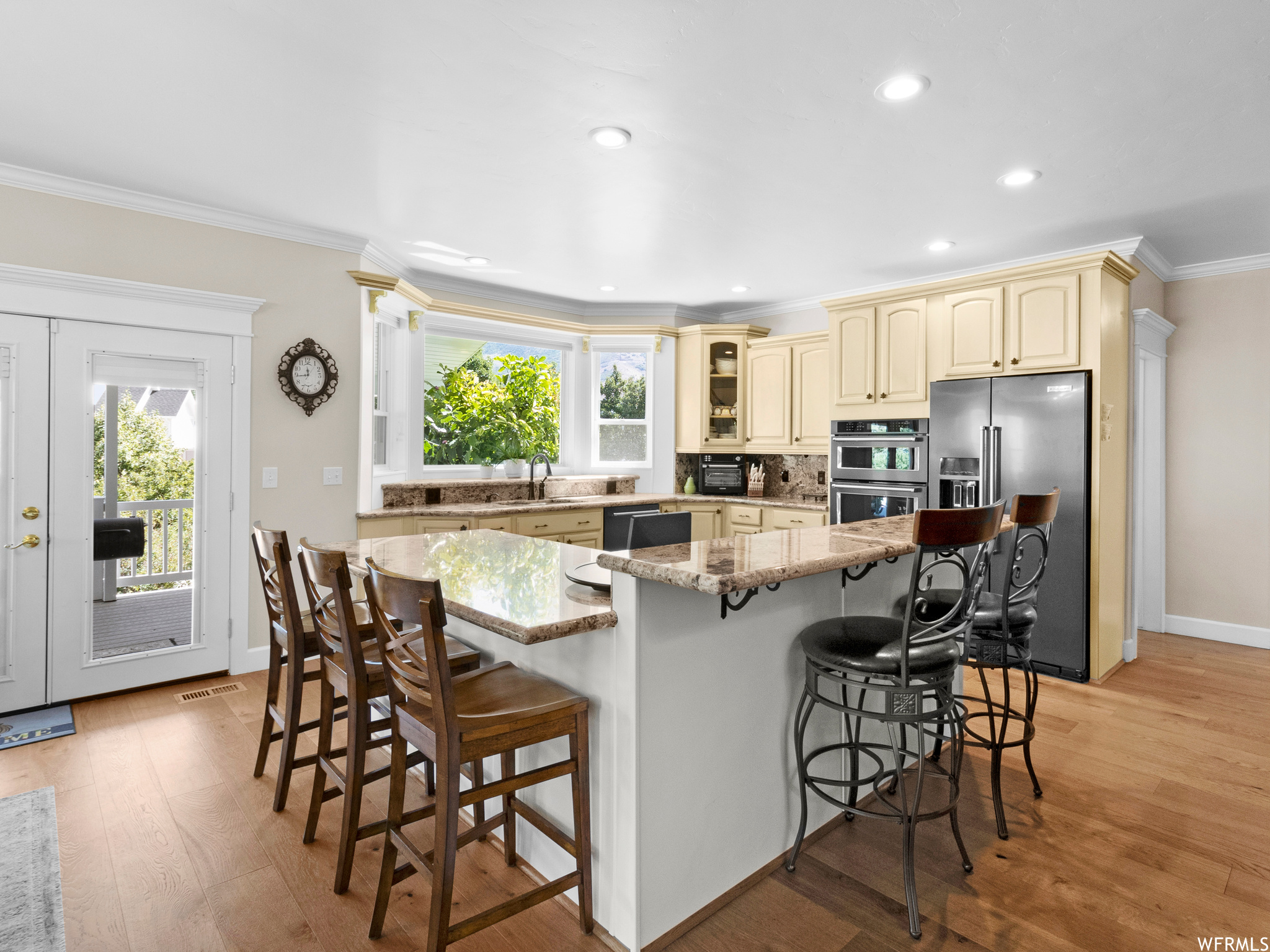 Kitchen featuring a wealth of natural light, ornamental molding, backsplash, appliances with stainless steel finishes, light hardwood flooring, and a center island