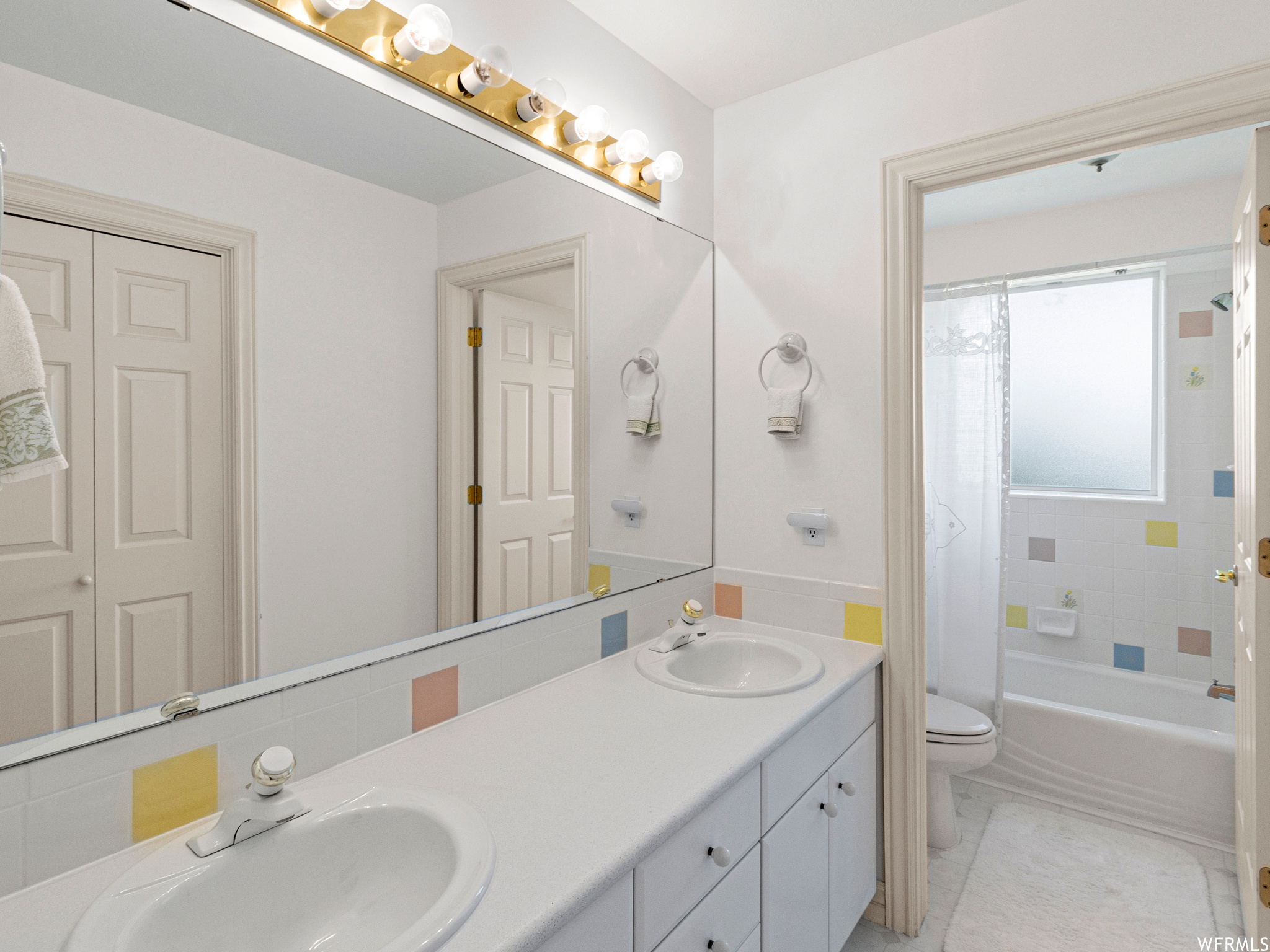Full bathroom with tiled shower / bath combo, dual large vanity, light tile flooring, and mirror