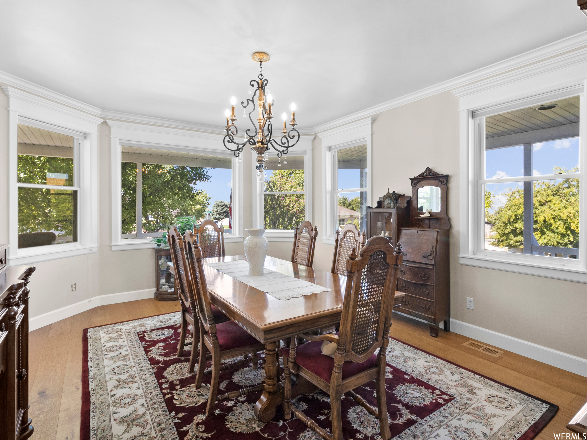 Wood floored dining area with a chandelier, ornamental molding, and a healthy amount of sunlight