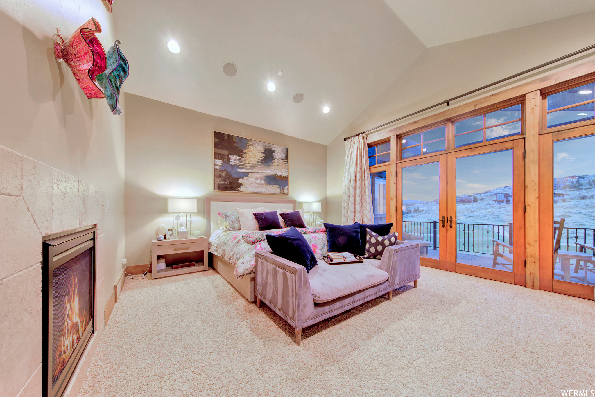 Main floor primary suite Bedroom with vaulted ceiling, light carpet, a fireplace, and french doors that lead out to a private deck.