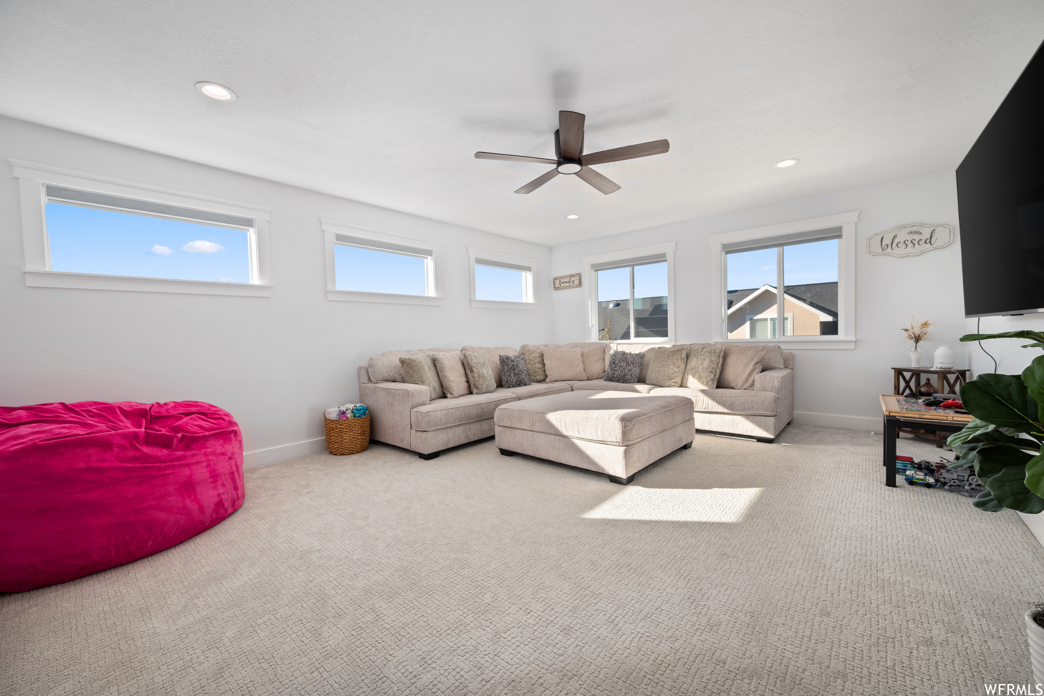 Carpeted second-floor living room with ceiling fan and abundant window light.