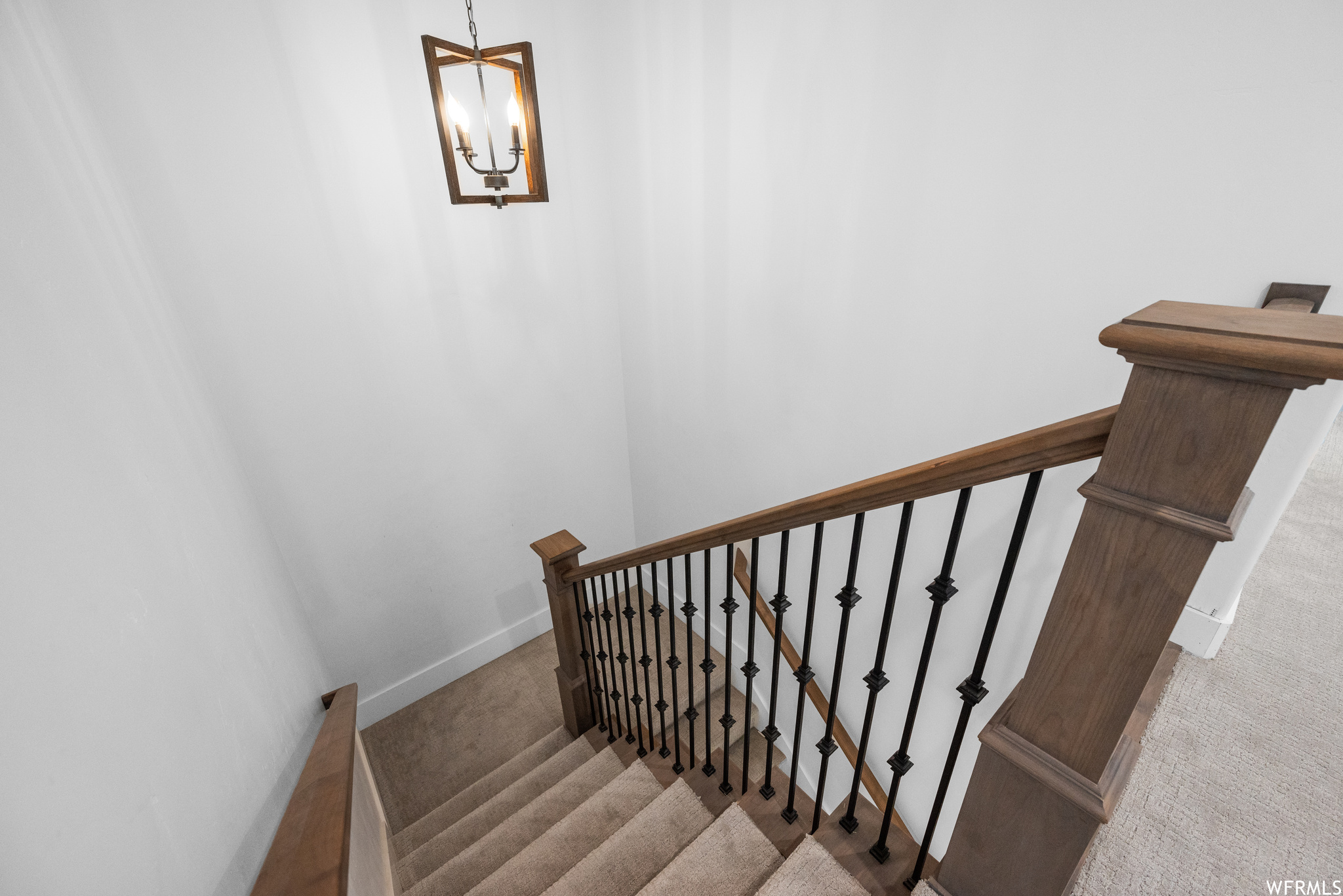 Stairs with carpet, a chandelier, and a stain-grade hardwood banister.