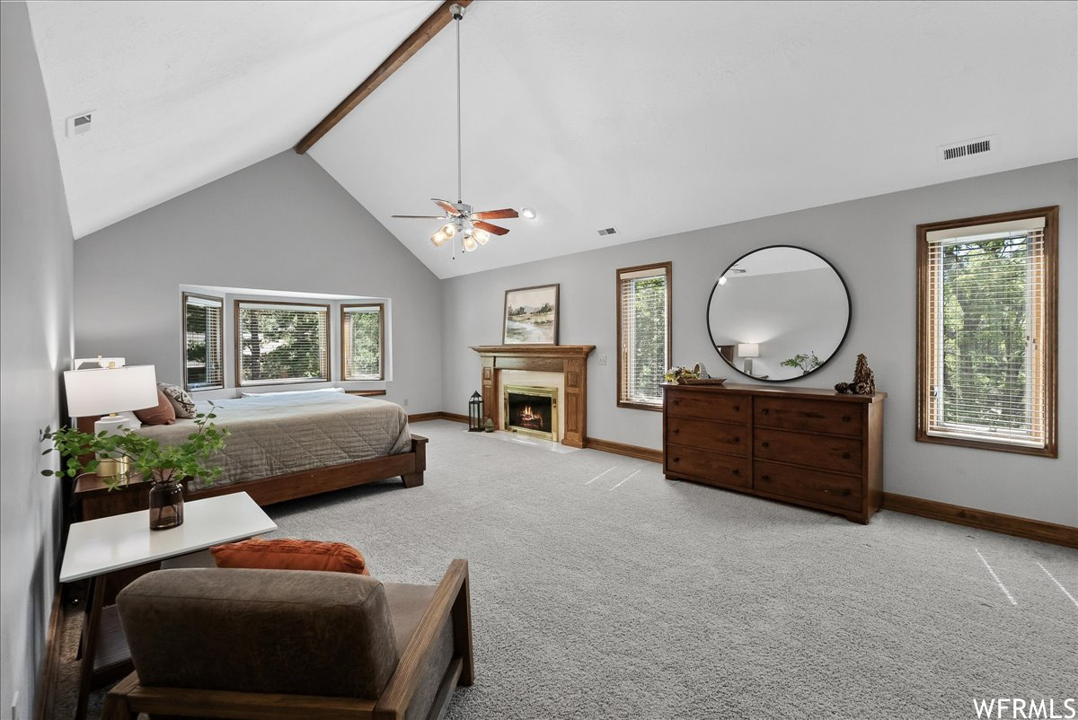 Carpeted bedroom featuring ceiling fan, lofted ceiling, a high ceiling, and a fireplace
