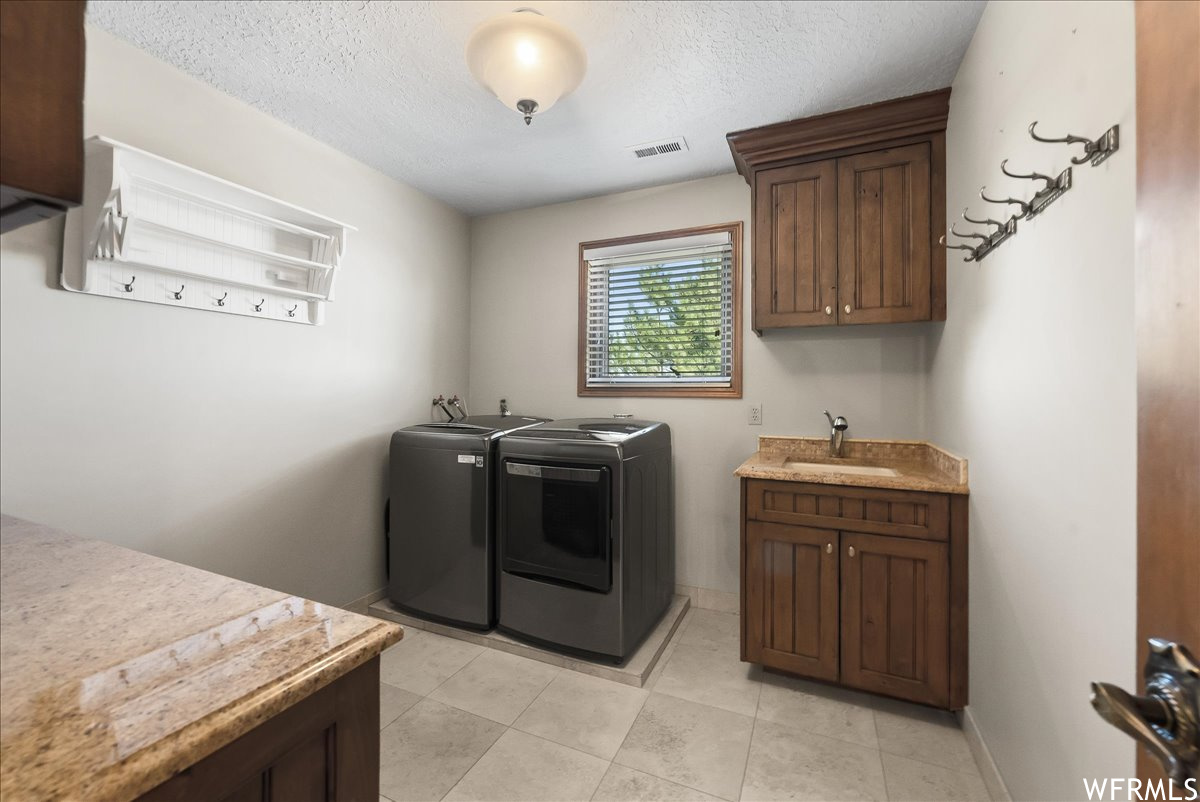Washroom featuring a textured ceiling, washing machine and clothes dryer, and light tile floors