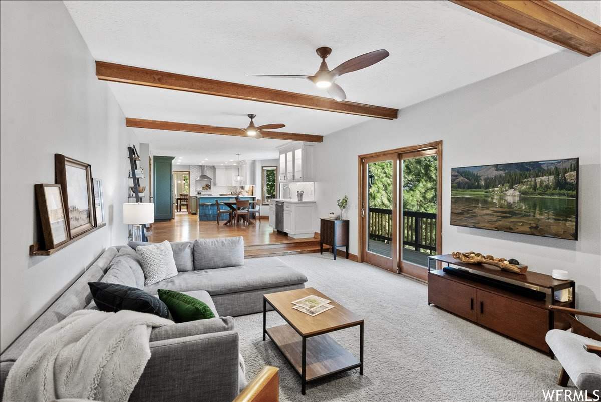 Carpeted living room featuring beamed ceiling and ceiling fan