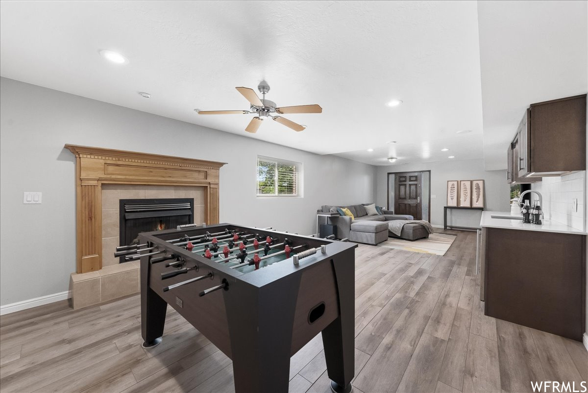 Rec room with a fireplace, light hardwood floors, and ceiling fan