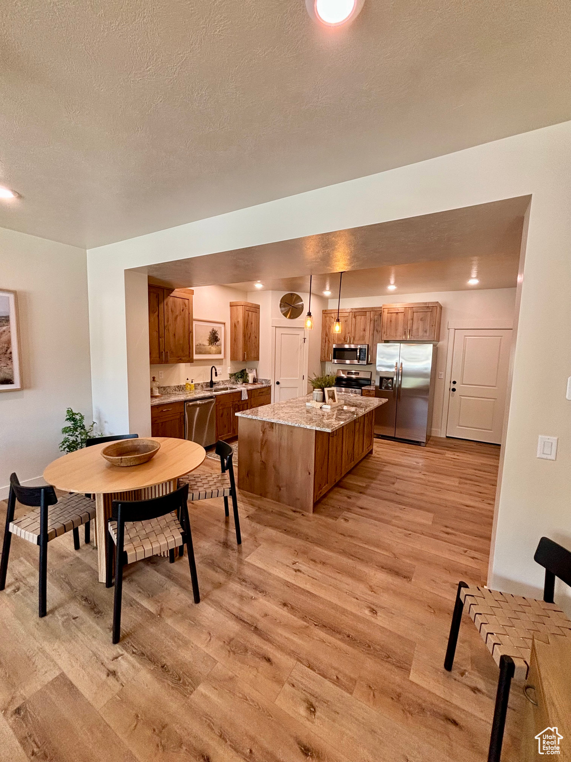 Kitchen with stainless steel appliances, a kitchen island, light wood-type flooring, and decorative light fixtures