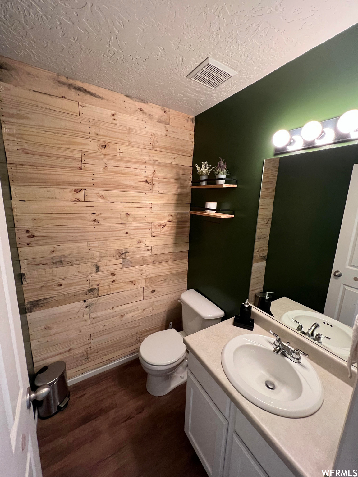 Bathroom with dark hardwood floors, a textured ceiling, mirror, vanity, and wooden walls