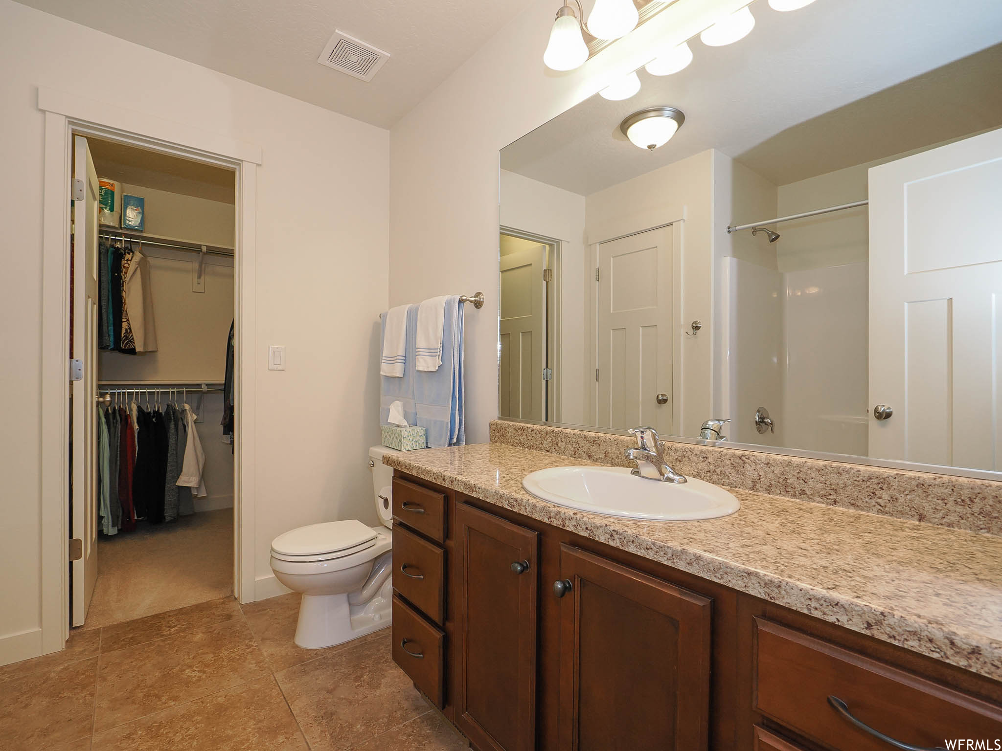 Bathroom featuring vanity with extensive cabinet space, mirror, and light tile floors
