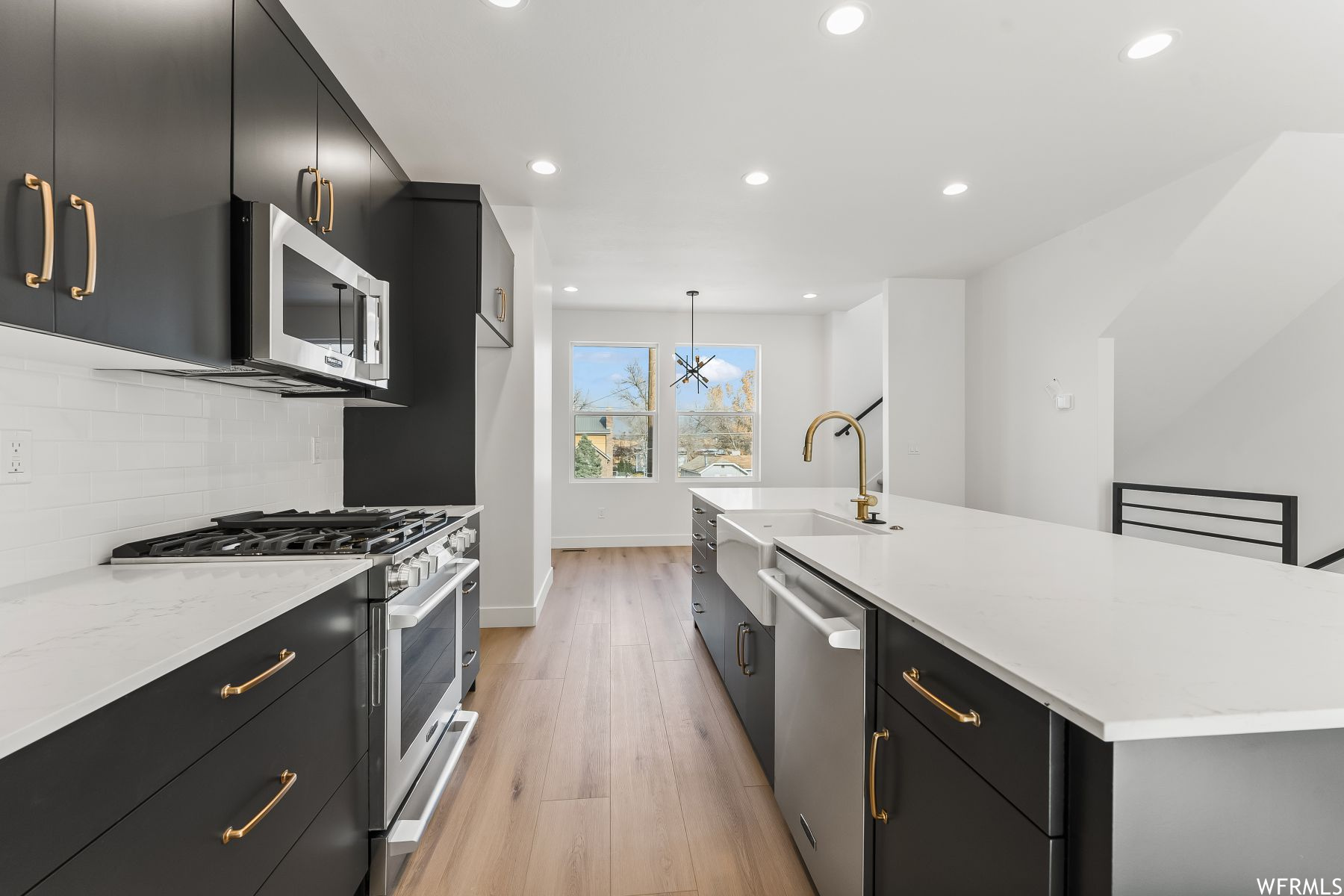 Kitchen featuring light hardwood / wood-style floors, pendant lighting, stainless steel appliances, tasteful backsplash, and an island with sink