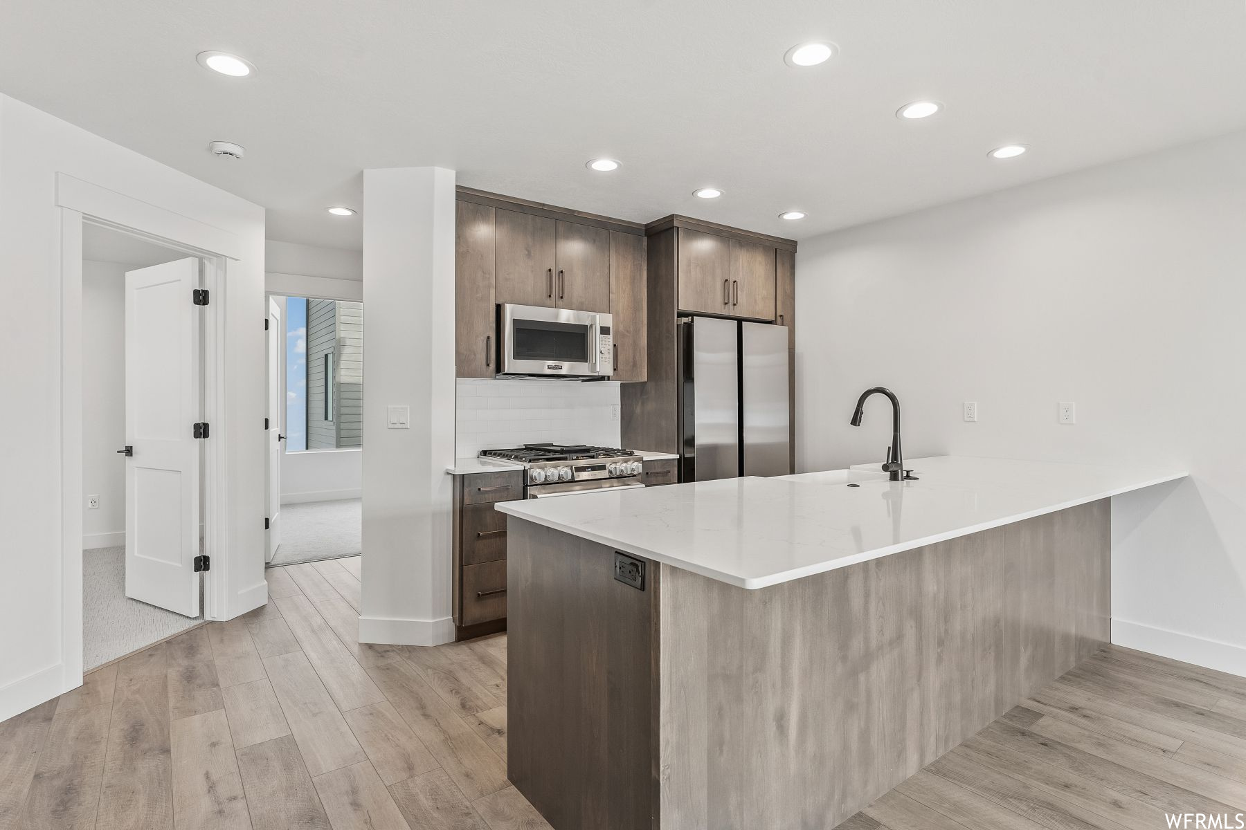 Kitchen with sink, light hardwood / wood-style flooring, stainless steel appliances, and backsplash