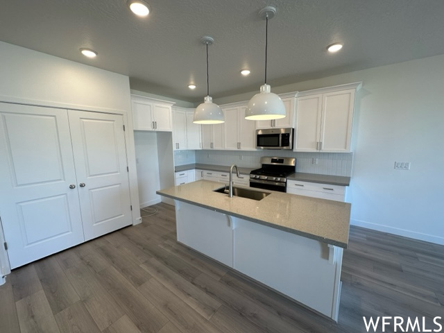 Kitchen featuring decorative light fixtures, backsplash, white cabinets, light countertops, appliances with stainless steel finishes, and laminate floors