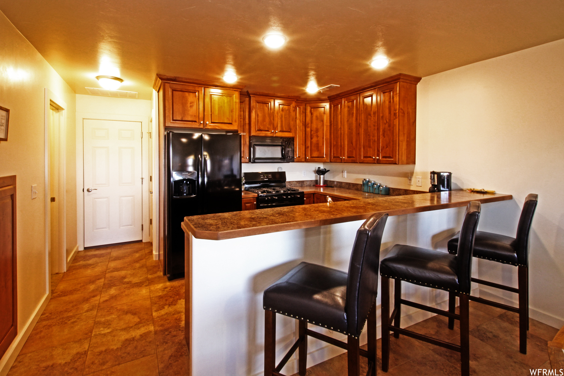 Kitchen with brown cabinets, black appliances, a center island, dark tile floors, and dark countertops