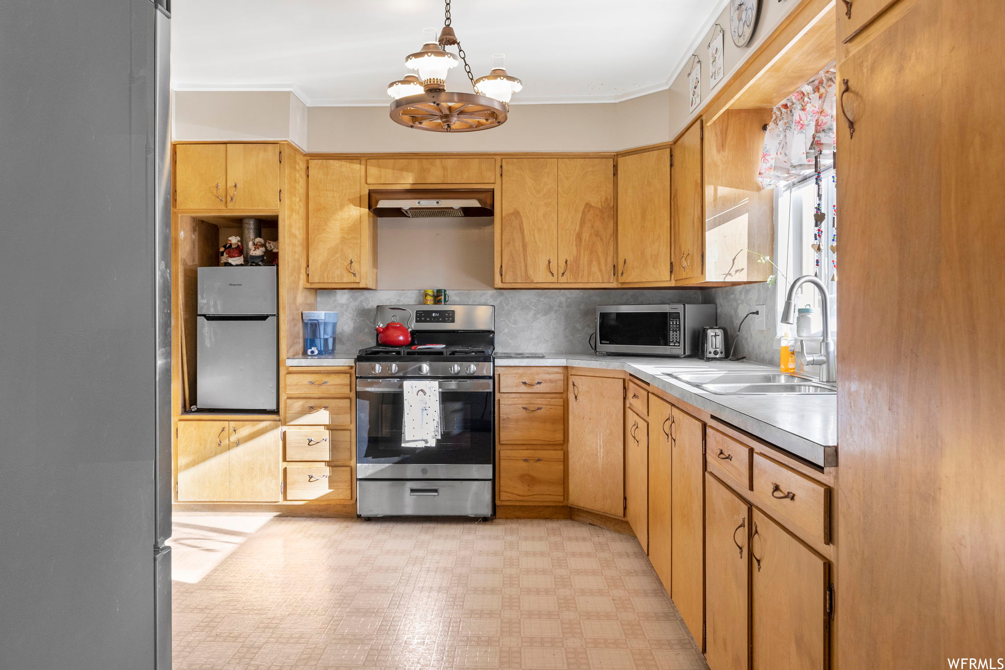 Kitchen with backsplash, ornamental molding, light tile flooring, and stainless steel appliances