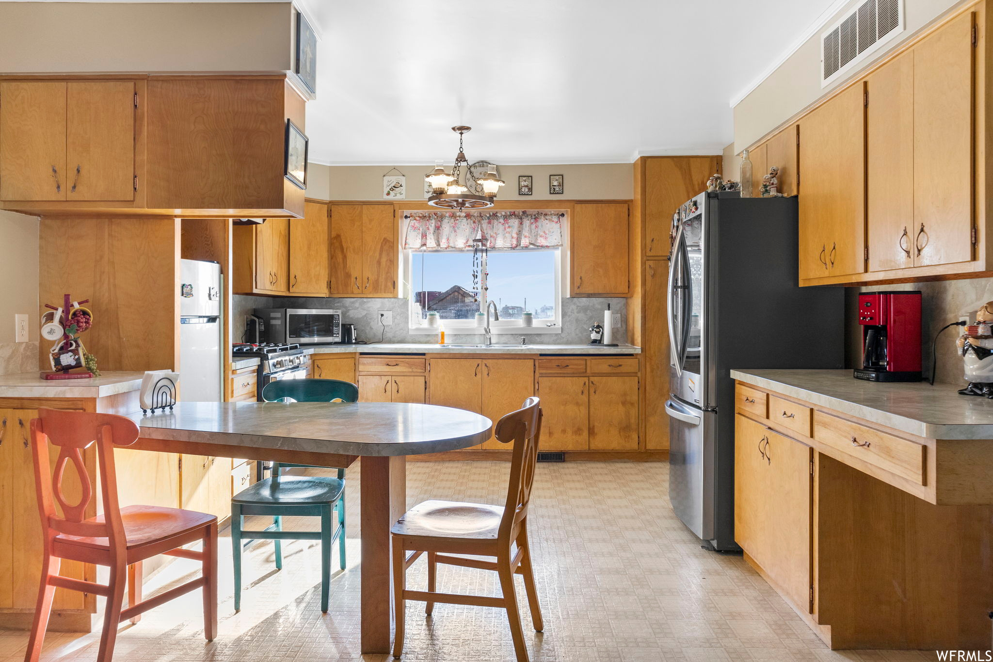 Kitchen featuring stacked washer and dryer, appliances with stainless steel finishes, brown cabinets, light countertops, and backsplash