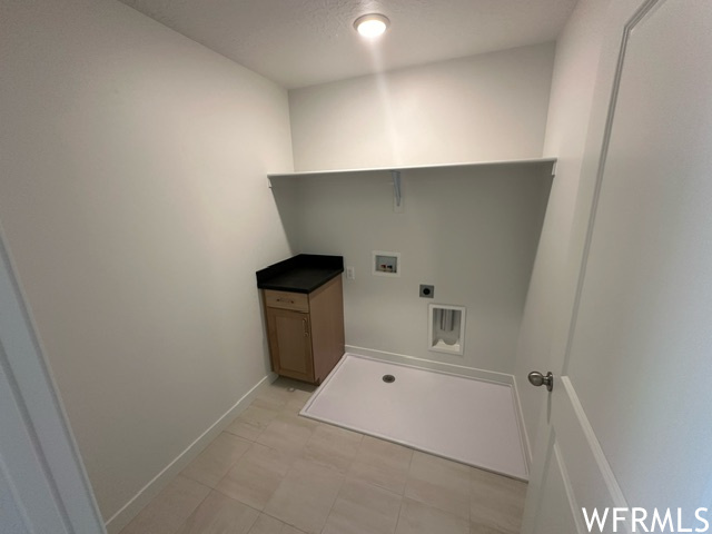Laundry room with tile flooring, cabinet with granite counter, upper supply shelf, and drain.