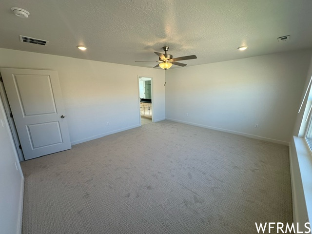 Master bedroom with light carpet flooring and fan with light.