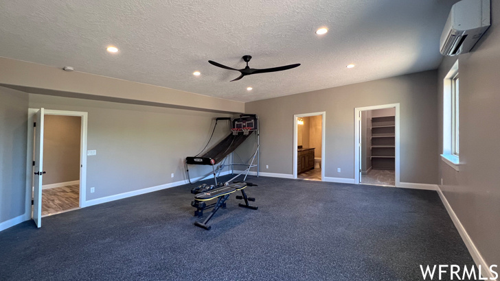 Workout room with ceiling fan, an AC wall unit, dark colored carpet, and a textured ceiling