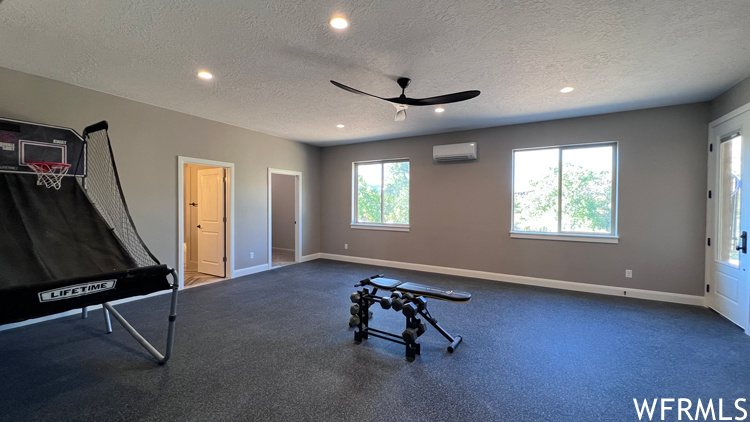 Exercise area with a textured ceiling, carpet flooring, a wall mounted AC, and ceiling fan