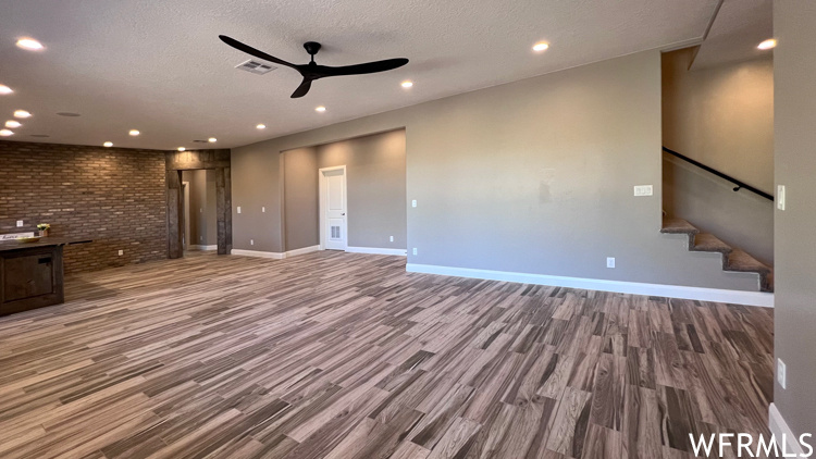 Unfurnished living room featuring dark hardwood flooring, ceiling fan, brick wall, and a textured ceiling