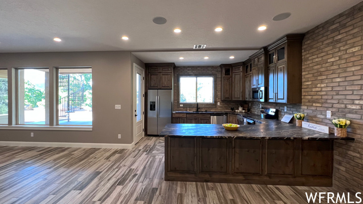 Kitchen with light hardwood flooring, dark stone countertops, tasteful backsplash, stainless steel appliances, and kitchen peninsula