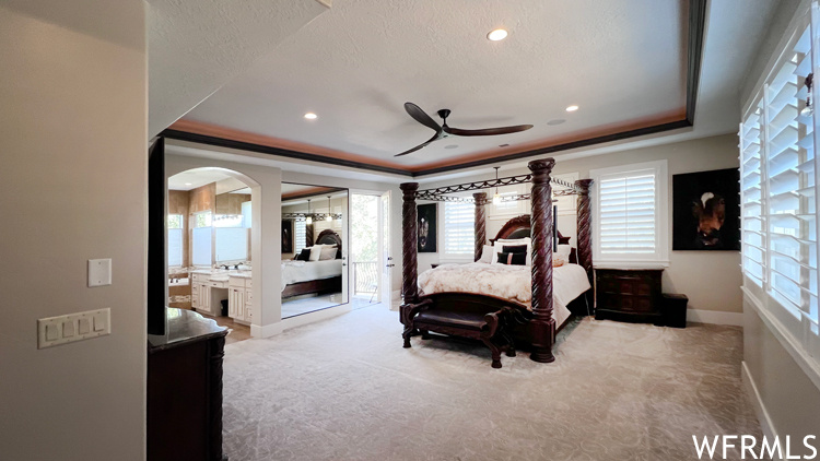 Bedroom with ceiling fan, a raised ceiling, light colored carpet, and access to outside