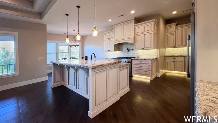 Kitchen with dark hardwood flooring, hanging light fixtures, a kitchen island with sink, and range