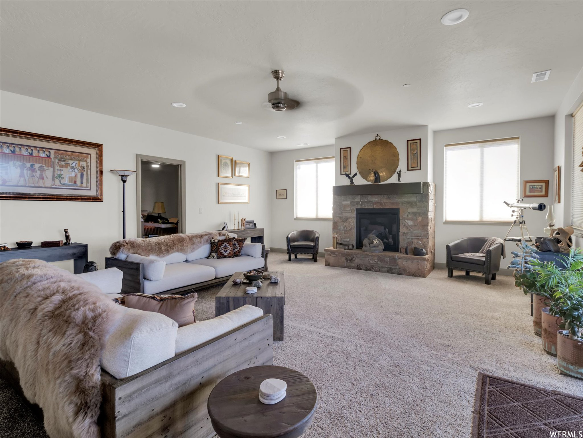 Living room with carpet floors, ceiling fan, and a stone fireplace