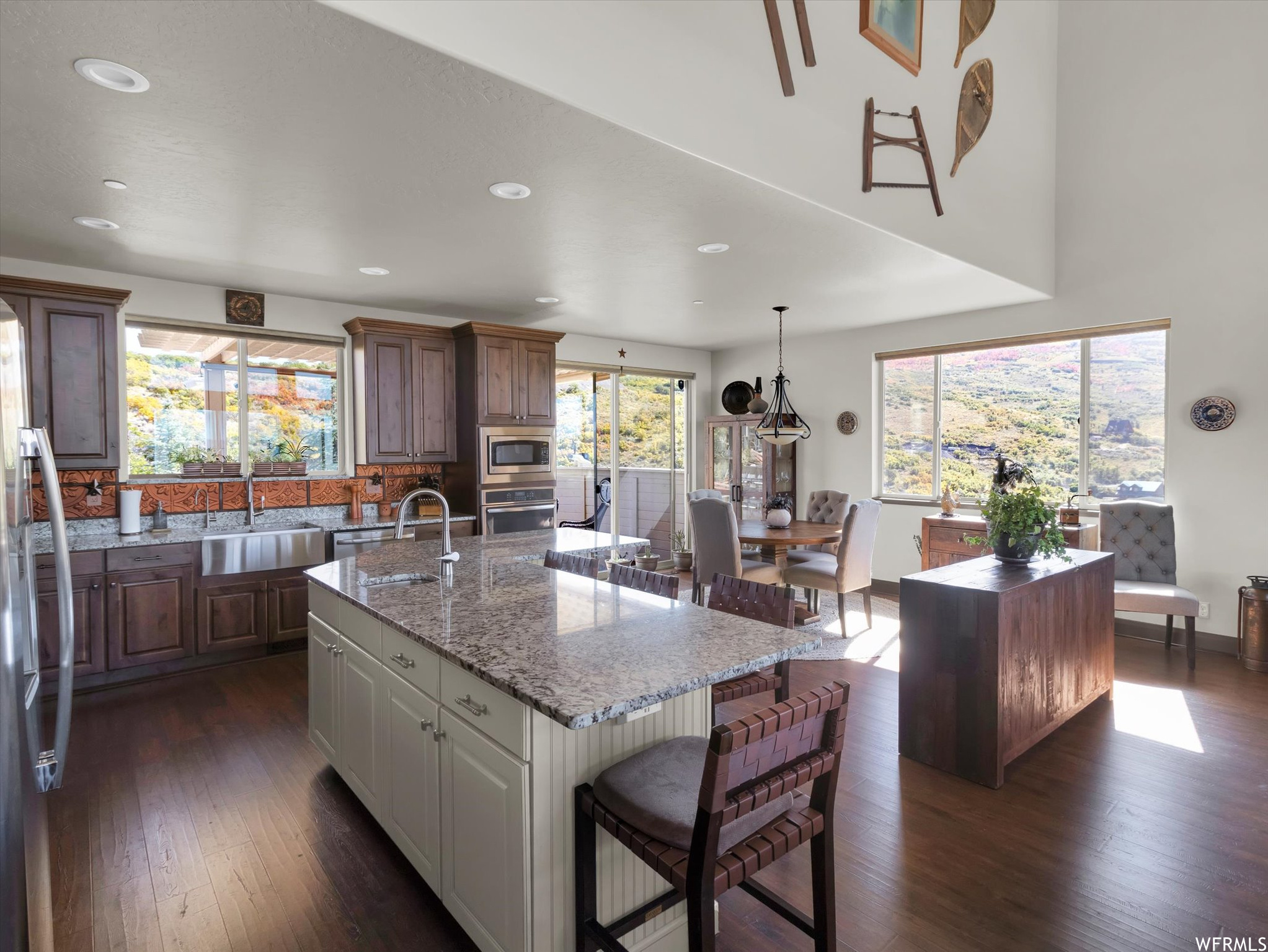 Kitchen featuring light stone countertops, a kitchen island with sink, dark hardwood floors, hanging light fixtures, and sink