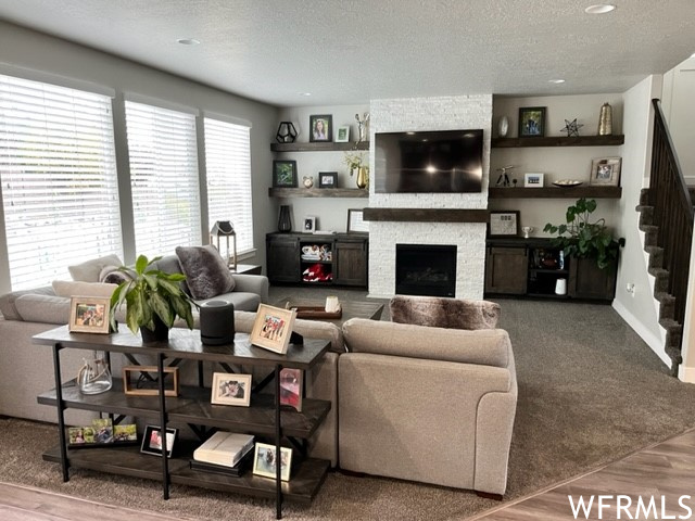 Living room featuring a textured ceiling, a fireplace, and carpet floors