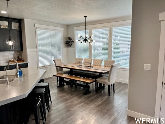 Dining room with a textured ceiling, a healthy amount of sunlight, hardwood flooring, and an inviting chandelier