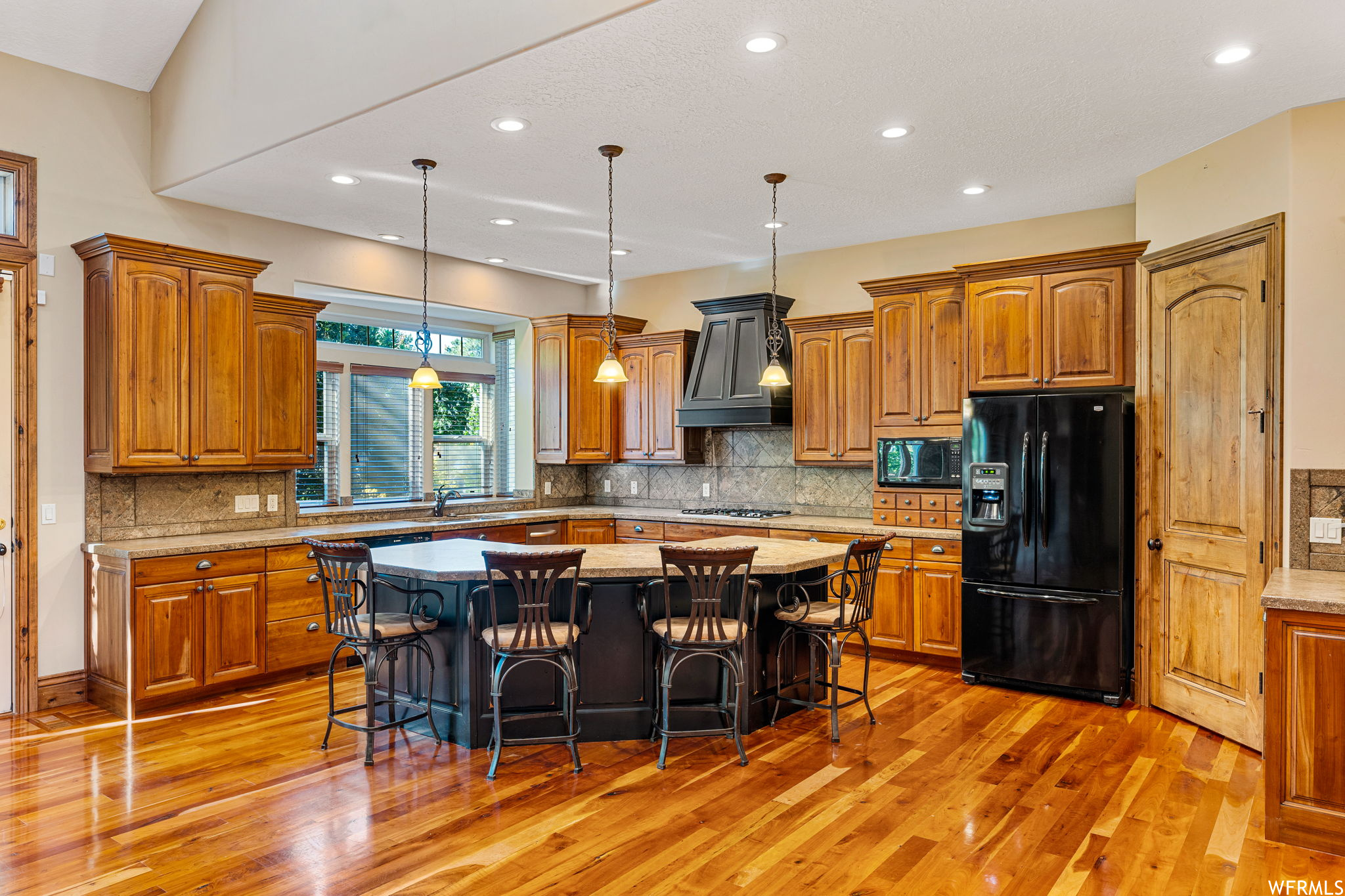 Kitchen featuring decorative light fixtures, premium range hood, a center island, and light hardwood floors