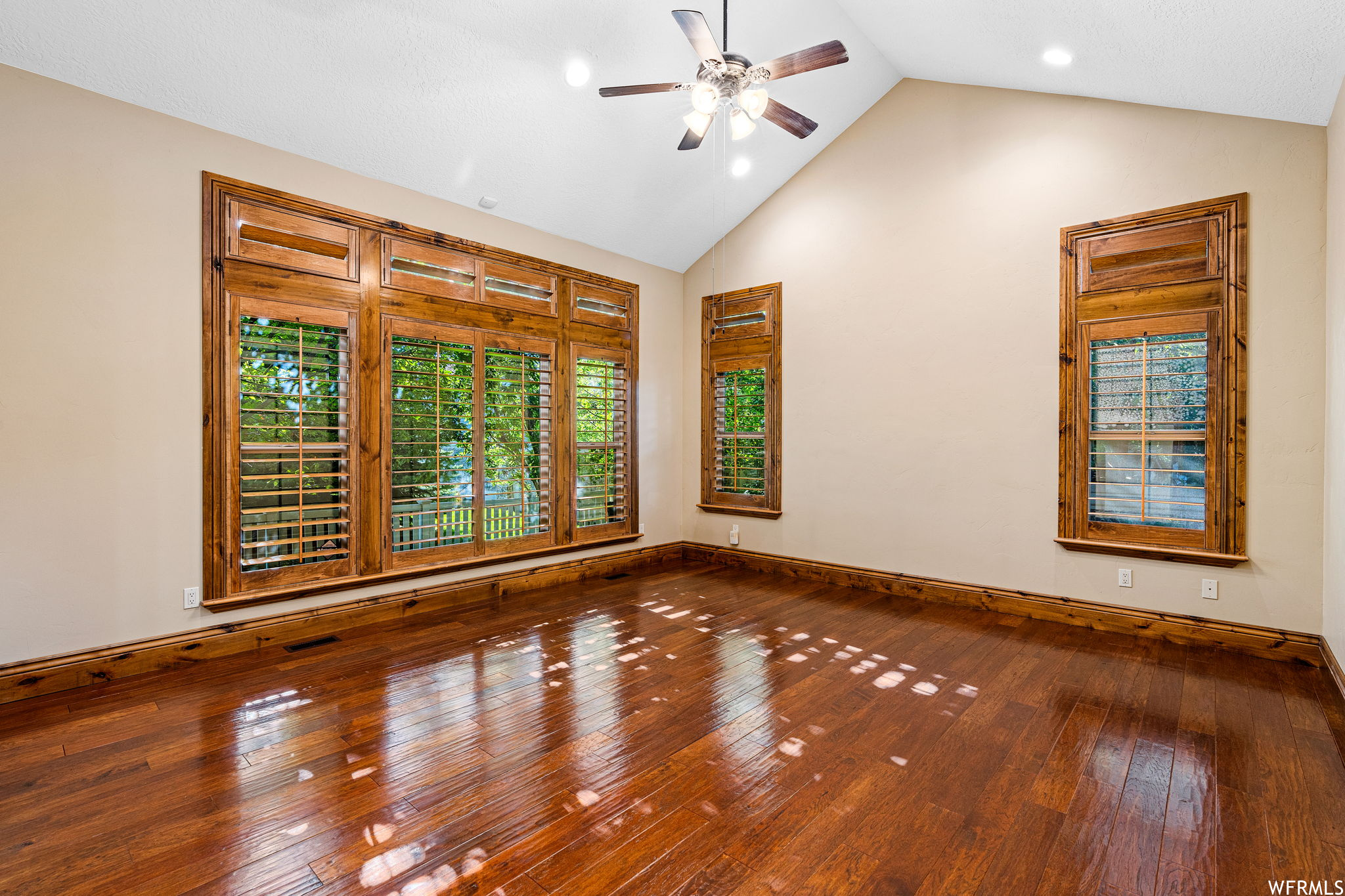 Hardwood floored empty room featuring vaulted ceiling and ceiling fan