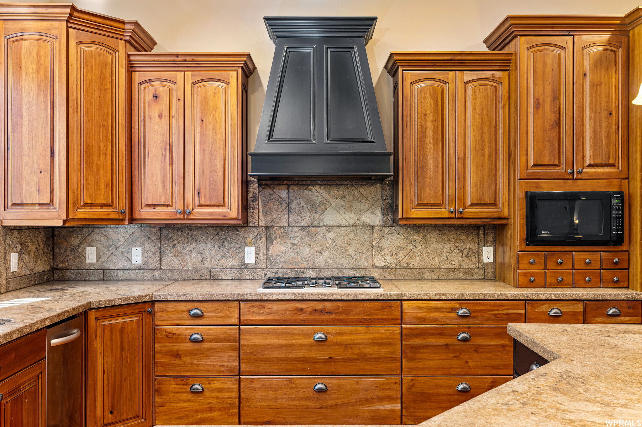 Kitchen with light stone counters, tasteful backsplash, custom range hood, and stainless steel gas cooktop