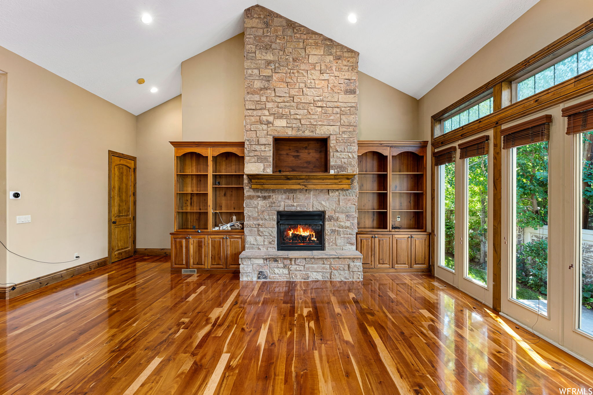 Unfurnished living room featuring a healthy amount of sunlight, hardwood floors, vaulted ceiling high, and a stone fireplace