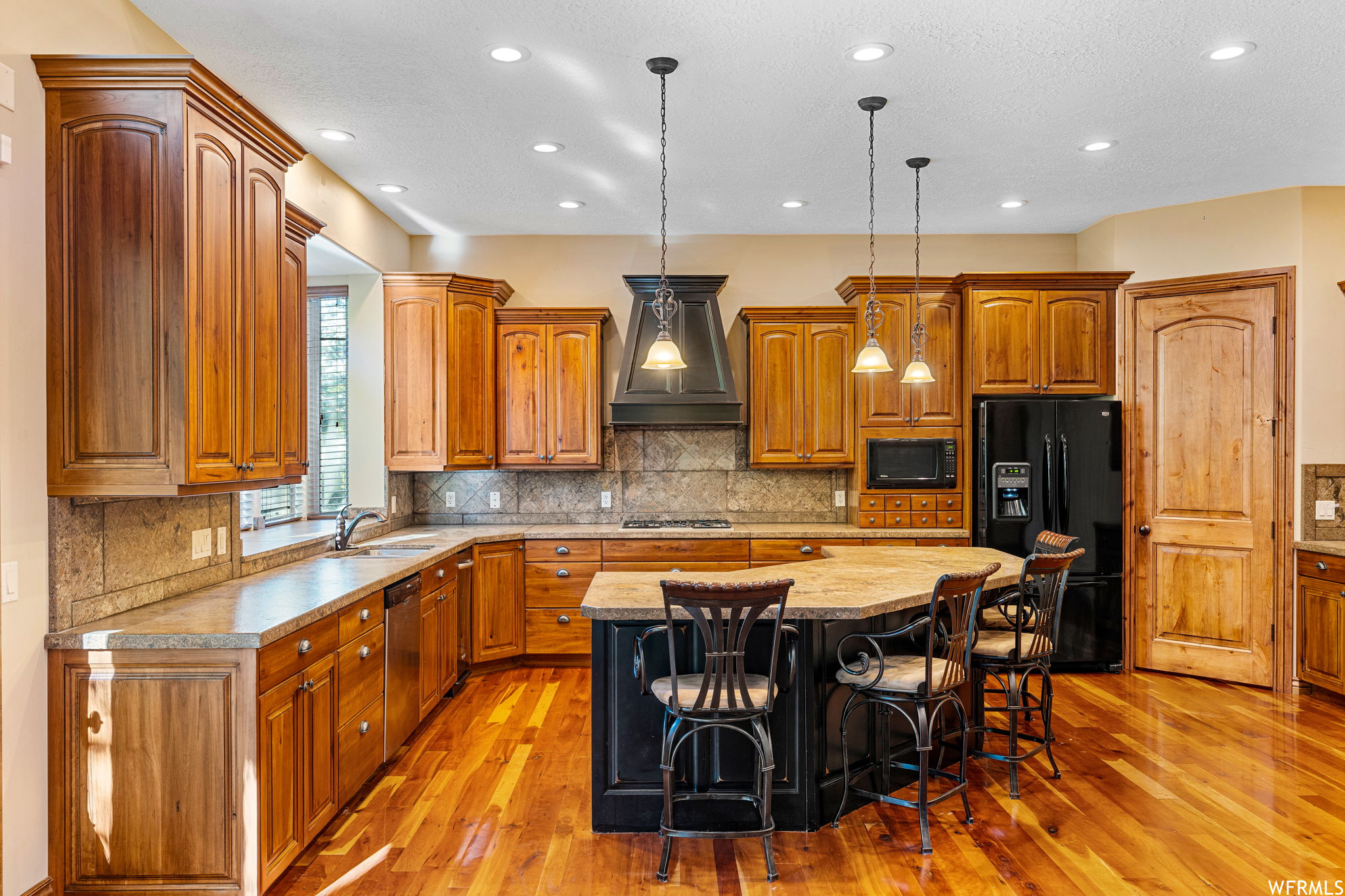 Kitchen with a center island, light hardwood flooring, premium range hood, hanging light fixtures, and backsplash