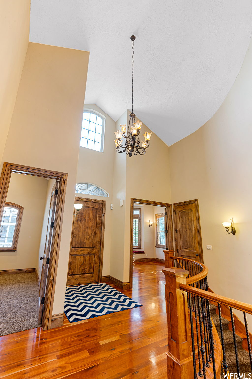 Hardwood floored foyer entrance featuring vaulted ceiling high, a notable chandelier, and a healthy amount of sunlight